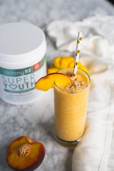 Mango smoothie with Super Youth Peach Mango collagen peptides sitting on a table.