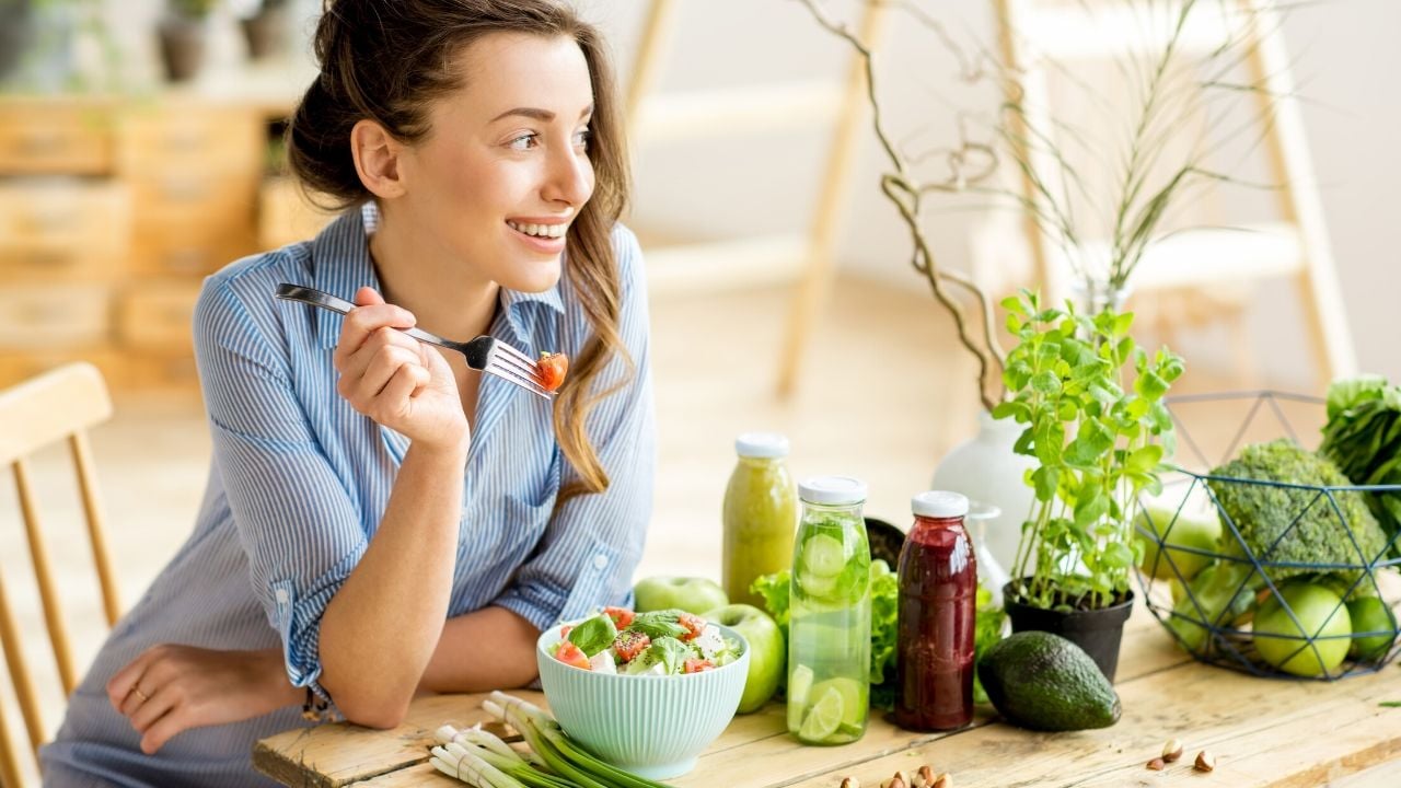 A woman smiling and eating a healthy meal made with SkinnyFit ingredients. Learning how to eat healthy on a budget is key to living a healthy lifestyle within your means.