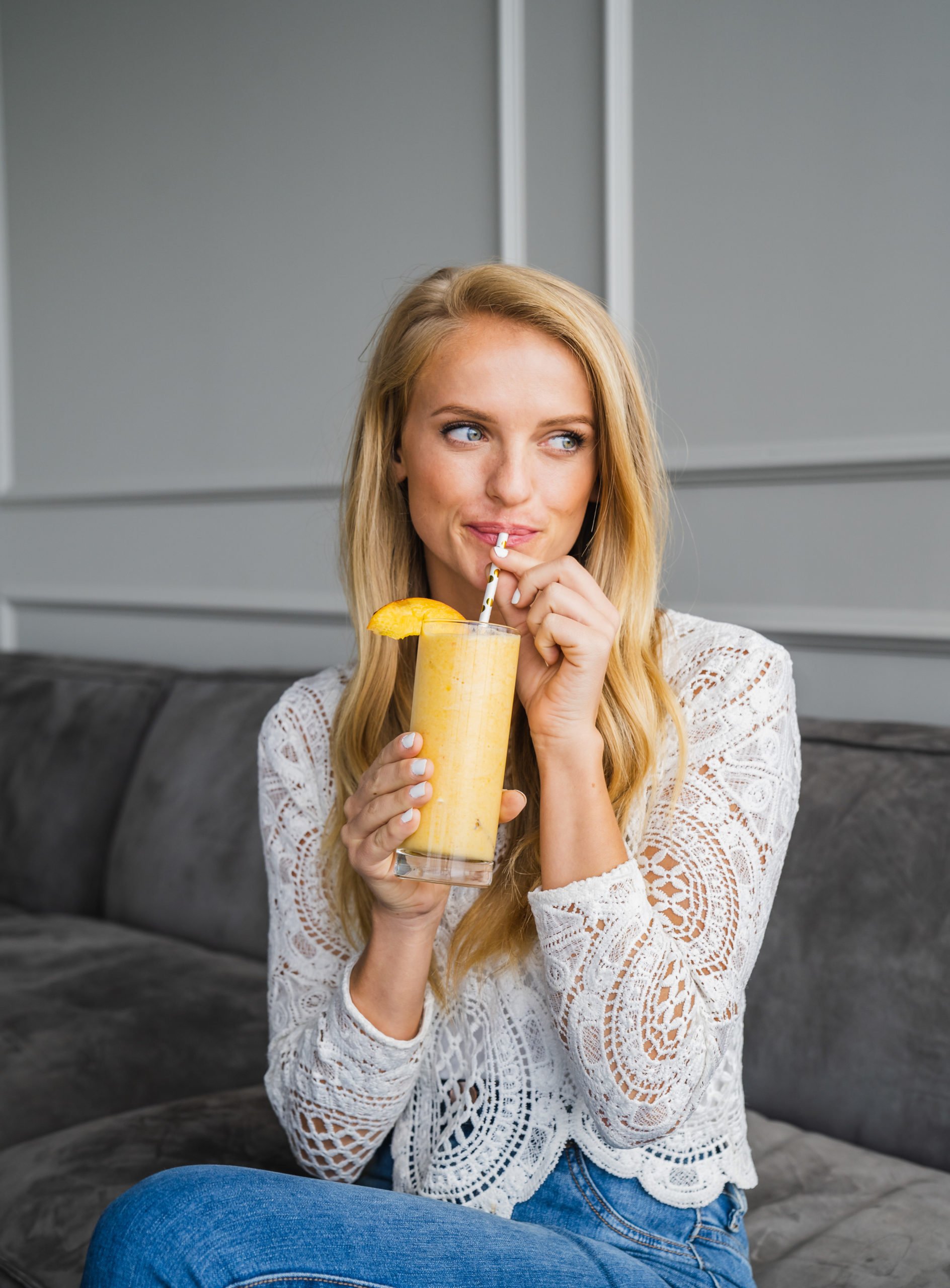 Woman sitting couch drinking a peach mango smoothie