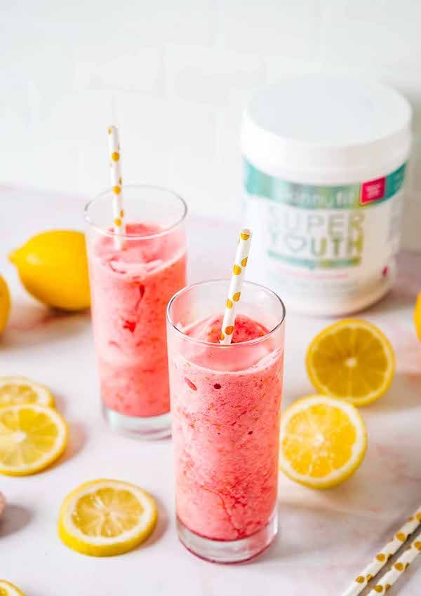 Two frozen lemonade slushies surrounded by lemon slices with a container of Super Youth collagen peptides in the background.