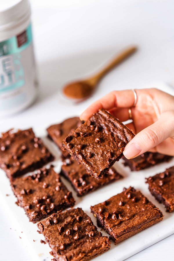 A hand holding on of the SkinnyFit Super Youth collagen healthy brownies, about to take a bite.