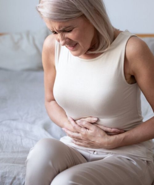 Woman sitting on her bed holding her stomach in discomfort