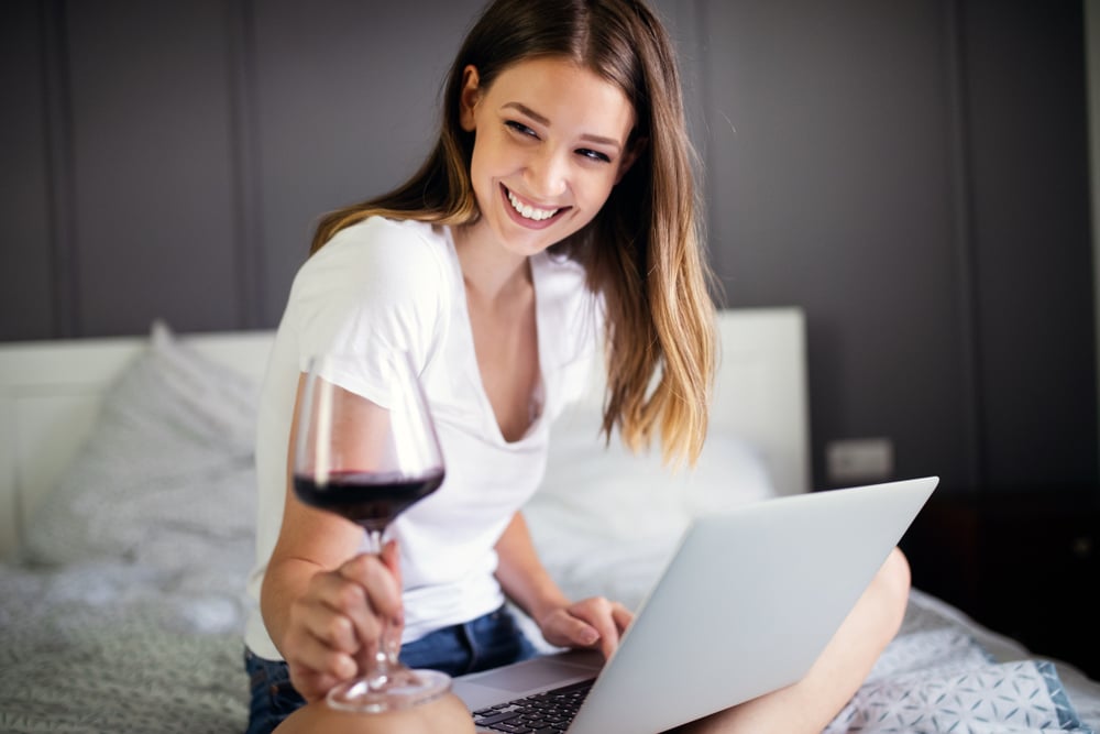 how many calories in wine? women sitting on bed drinking red wine