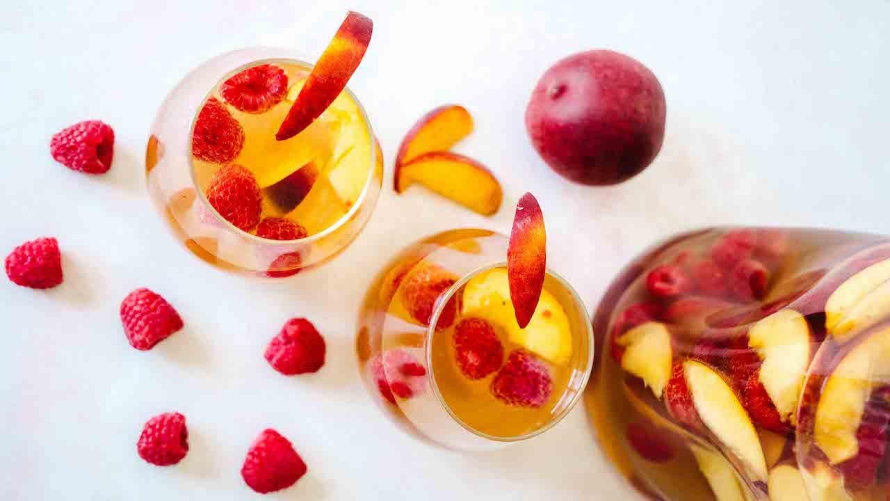 Peach rosé sangria surrounded by fresh raspberries and peaches.