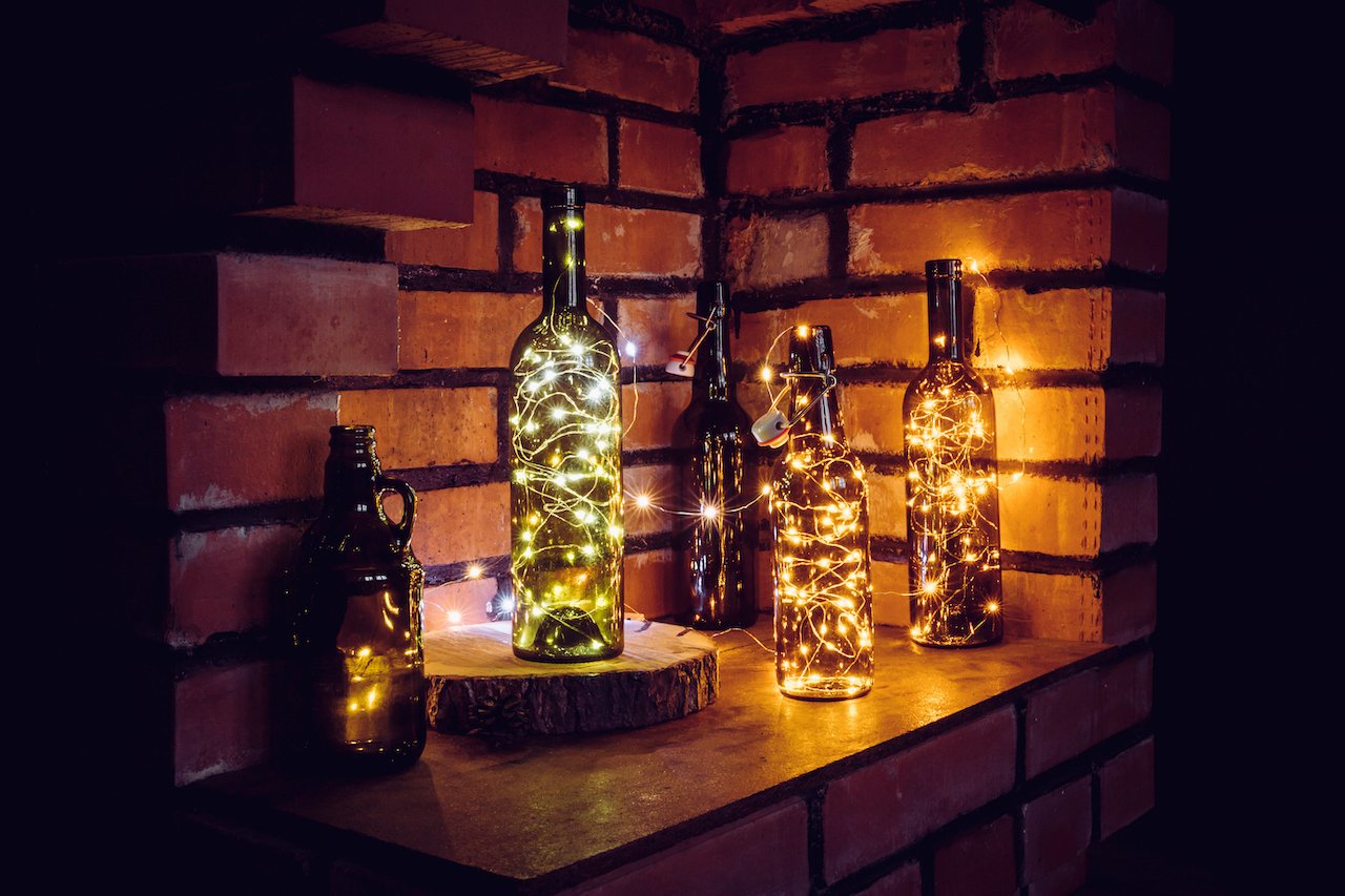 String lights wrapped around and inside wine and beer bottles for a cozy, ambient setting.