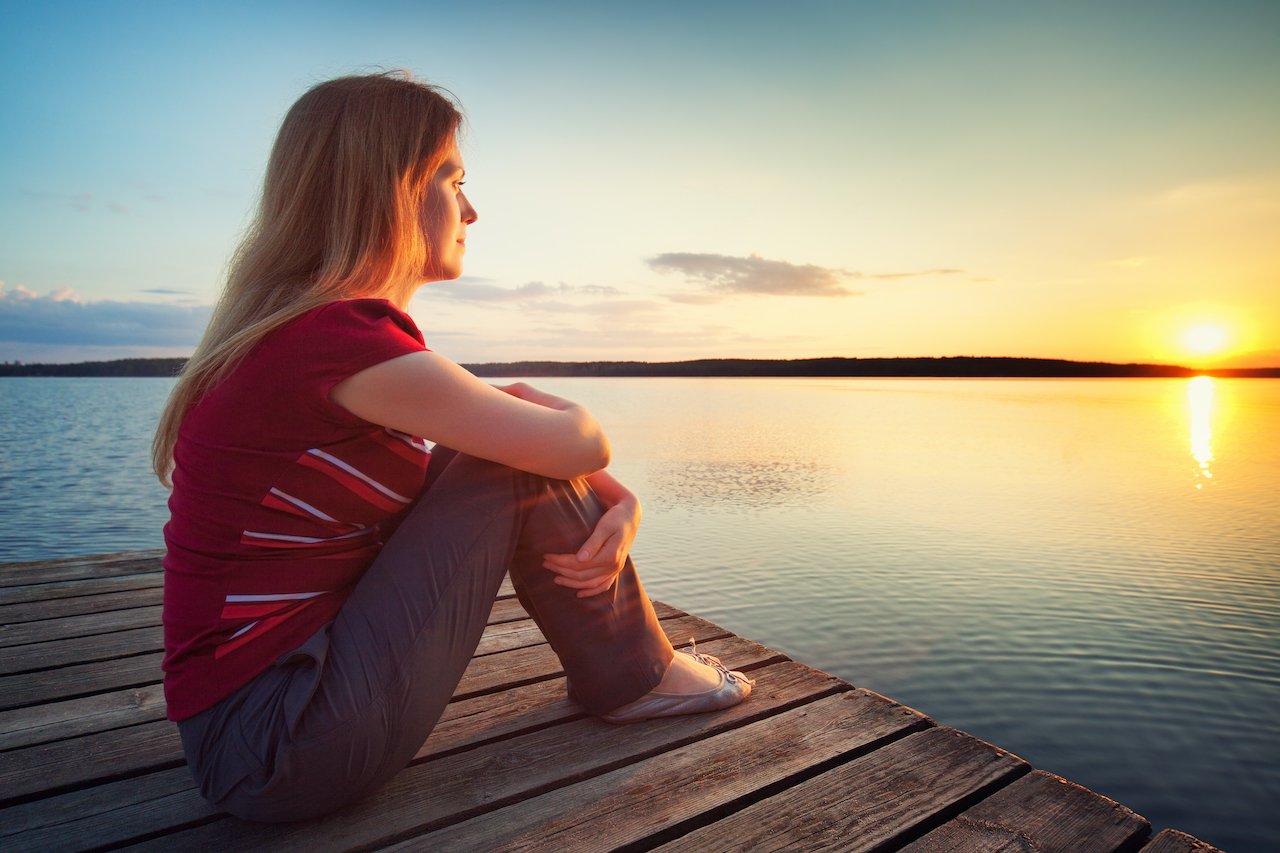 Woman sitting on a dock meditating and gazing at the water.
