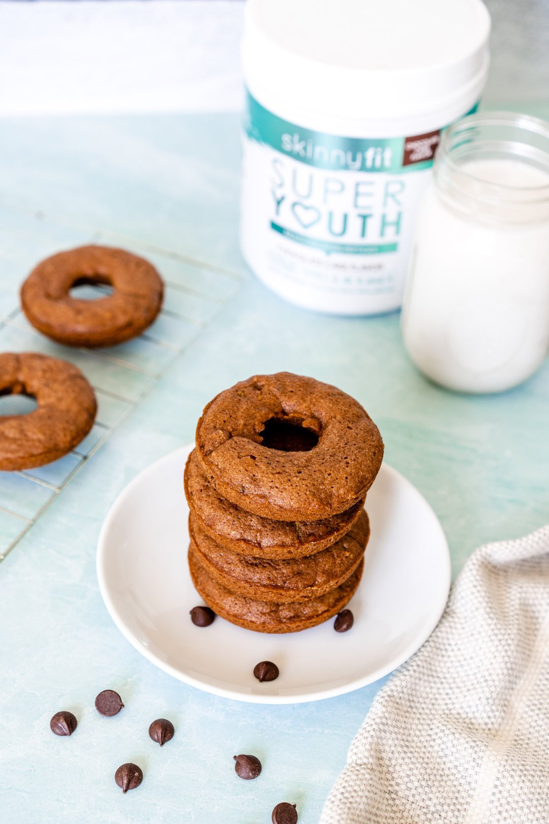 A stack of zucchini baked donuts on a plate with SkinnyFit Super Youth Collagen Peptides and a glass of milk
