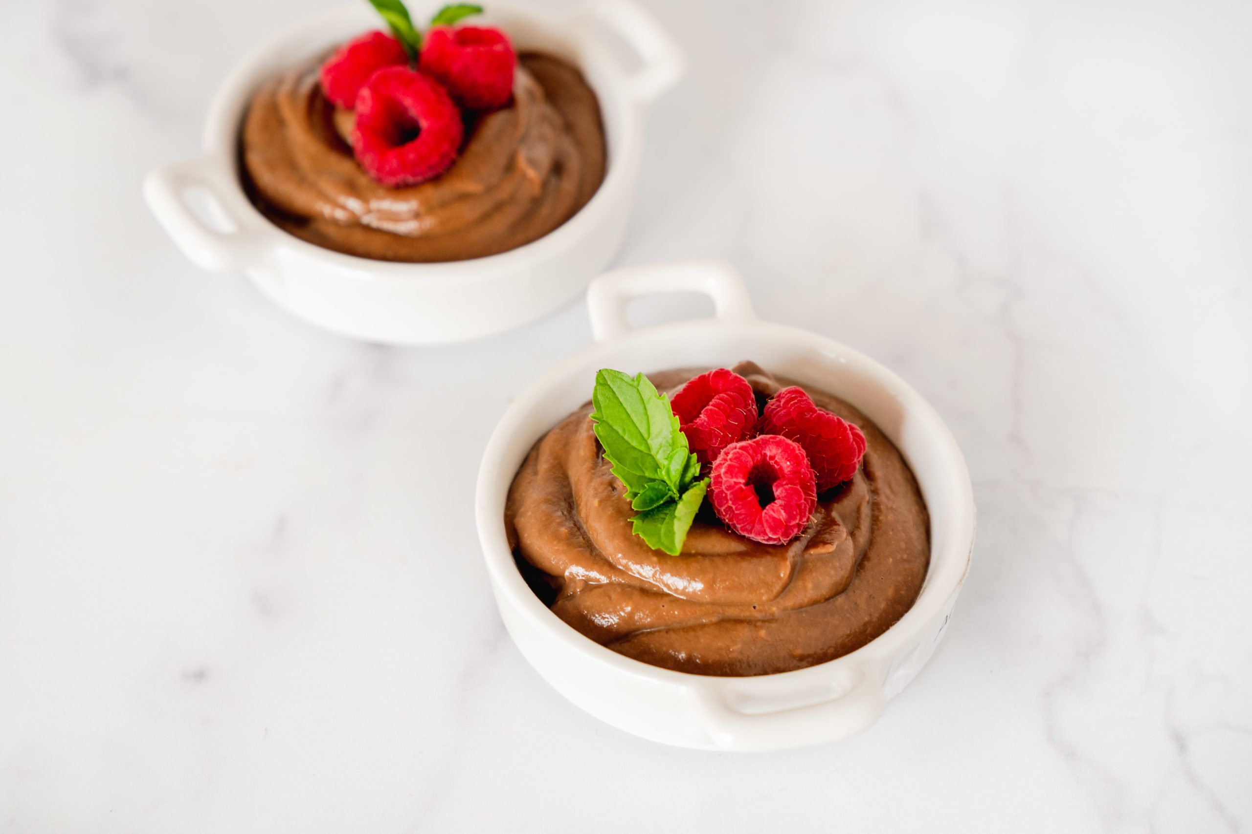 Two servings of avocado chocolate mousse with SkinnyFit Chocolate Cake collagen peptides in white porcelain cups. 