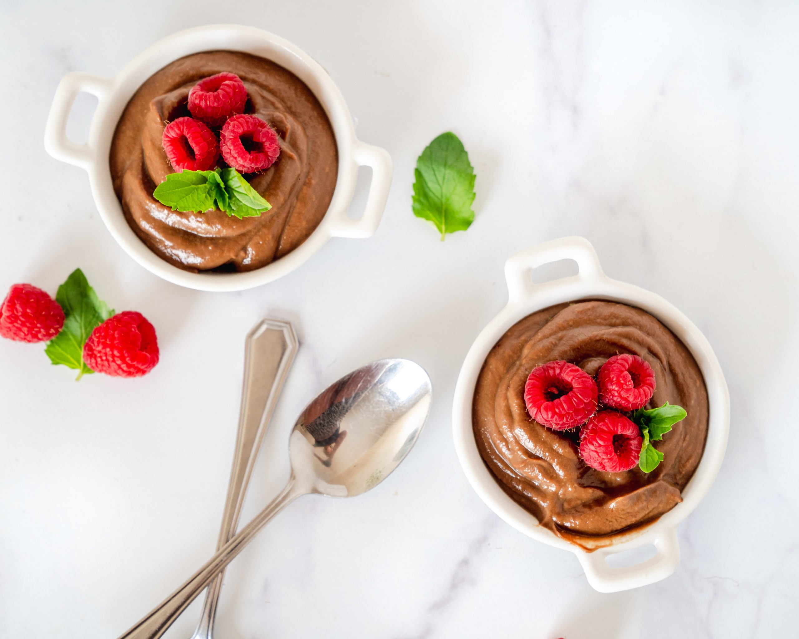 Two helpings avocado chocolate mousse with SkinnyFit Chocolate Cake collagen peptides in white porcelain cups with silver spoons for the perfect display.