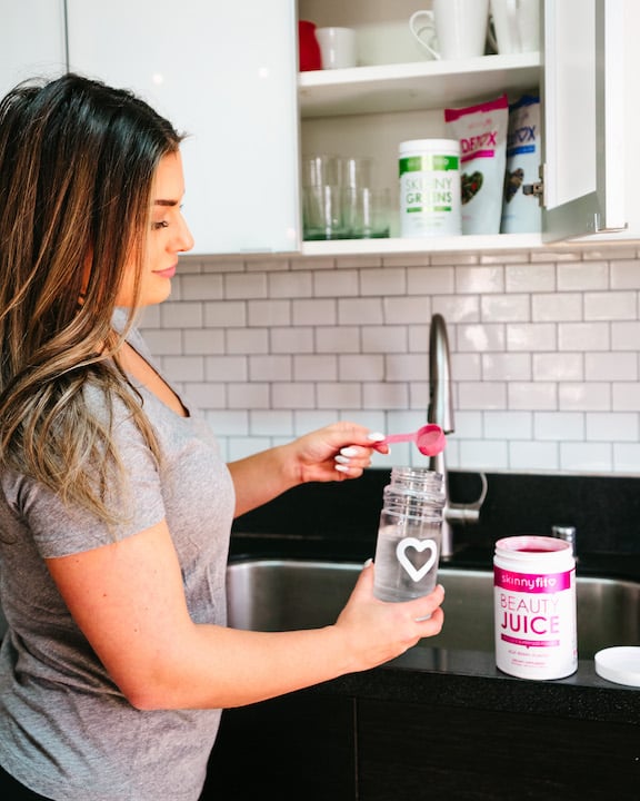 Woman pouring water into SkinnyFit Beauty Juice to help stay hydrated, which is important to do if you're wondering why are my lips so dry