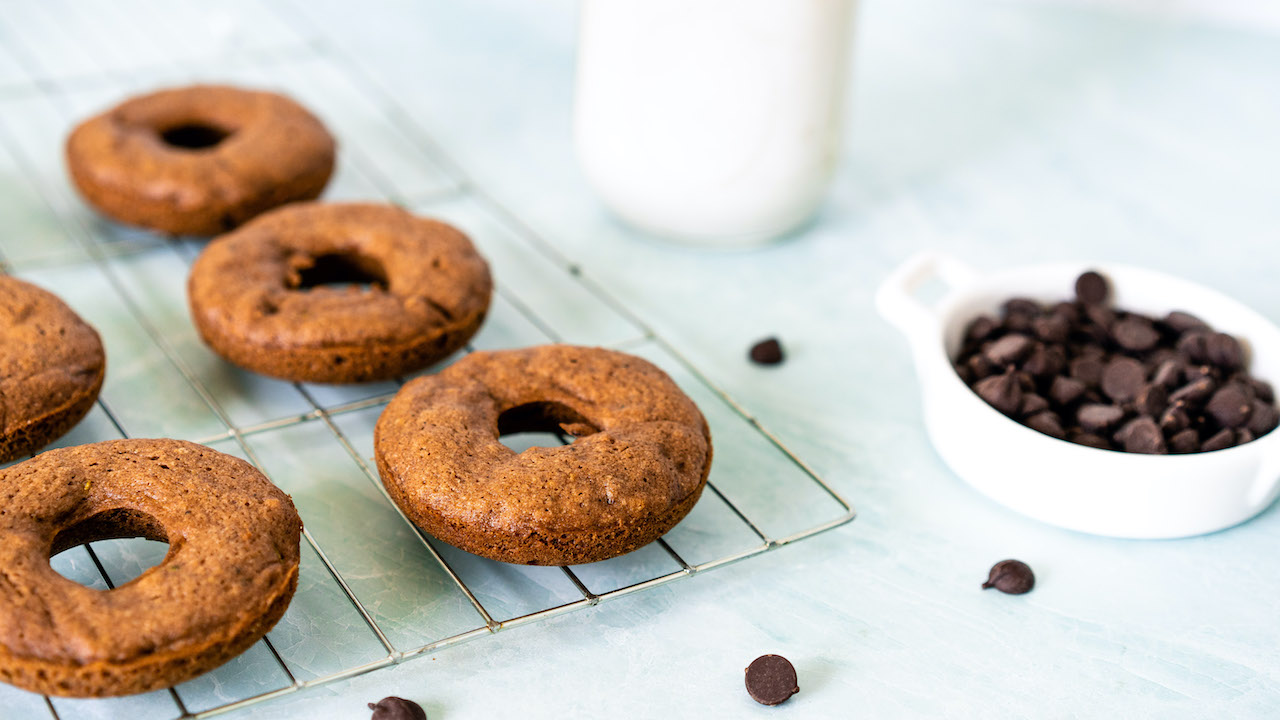 Healthy baked donuts with SkinnyFit Super Youth Chocolate Cake collagen on a counter with chocolate chips and milk