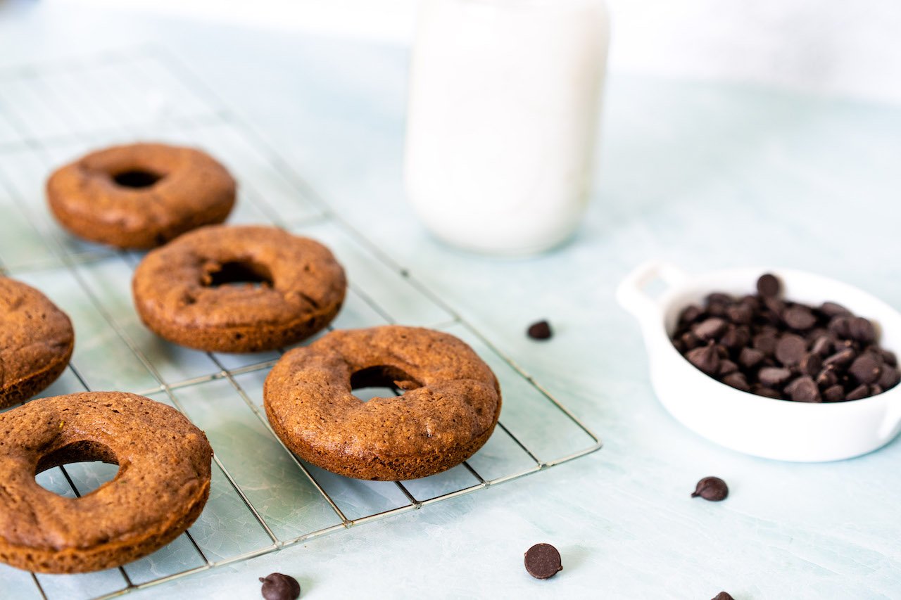 Delicious, healthy baked donuts made with SkinnyFit Super Youth Chocolate Cake Collagen peptides on a tray with chocolate chips and milk. 