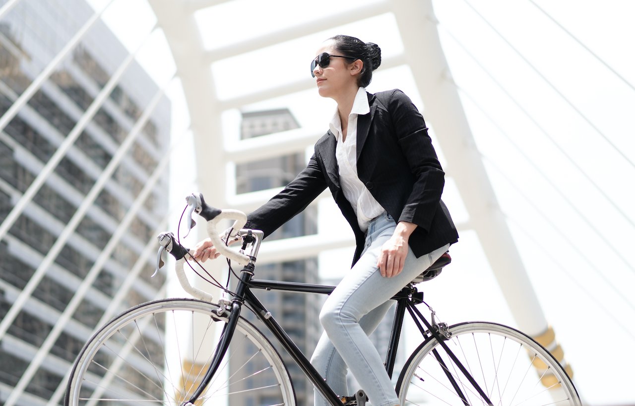 A business woman riding her bike to work, which is a good way to fit exercise into your day and break through weight loss plateau.