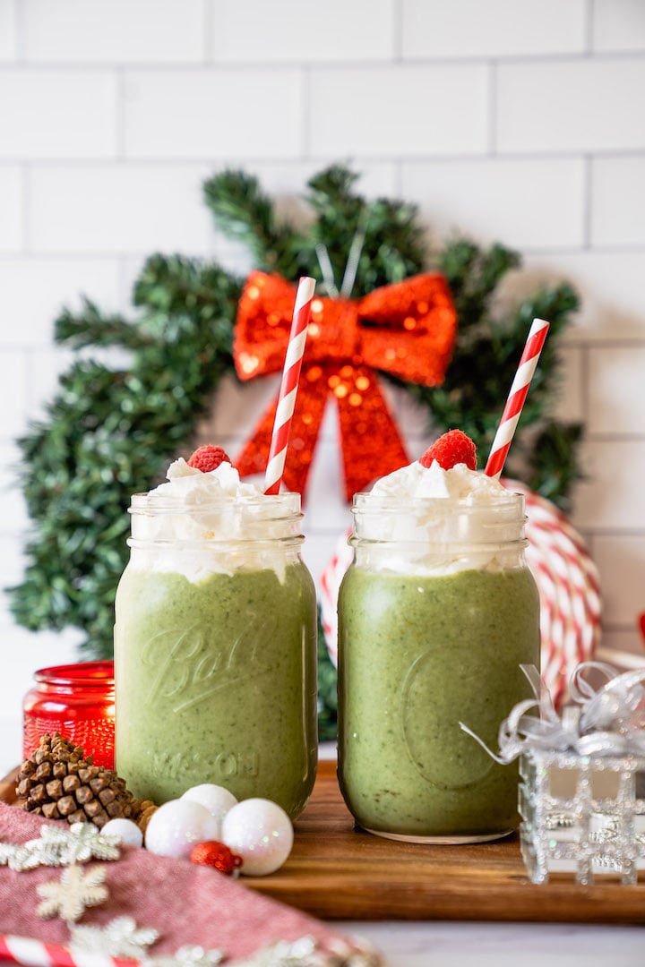 Two green Grinch smoothies with SkinnyFit Skinny Greens superfood powder, surrounded by a wreath and other holiday decorations.