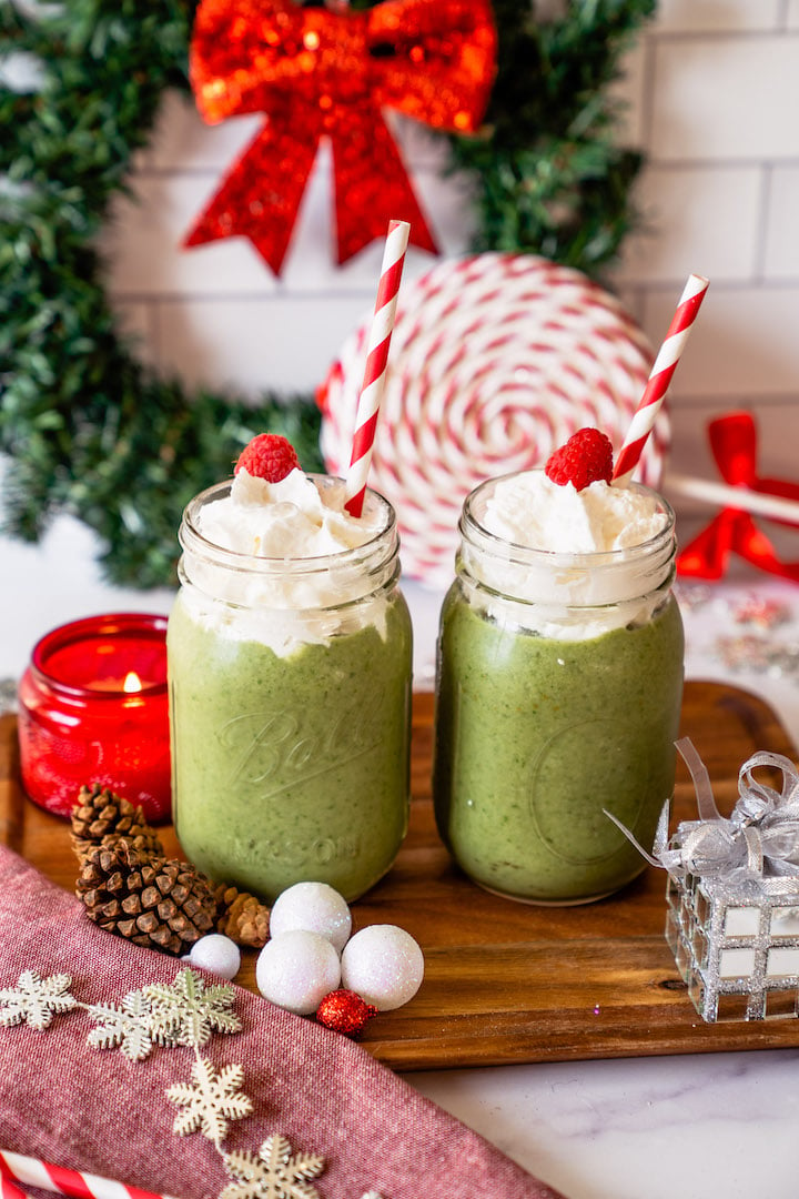Two mason jars of Green Grinch smoothie with SkinnyFit Skinny Greens with a candy cane lollipop and other holiday decorations.